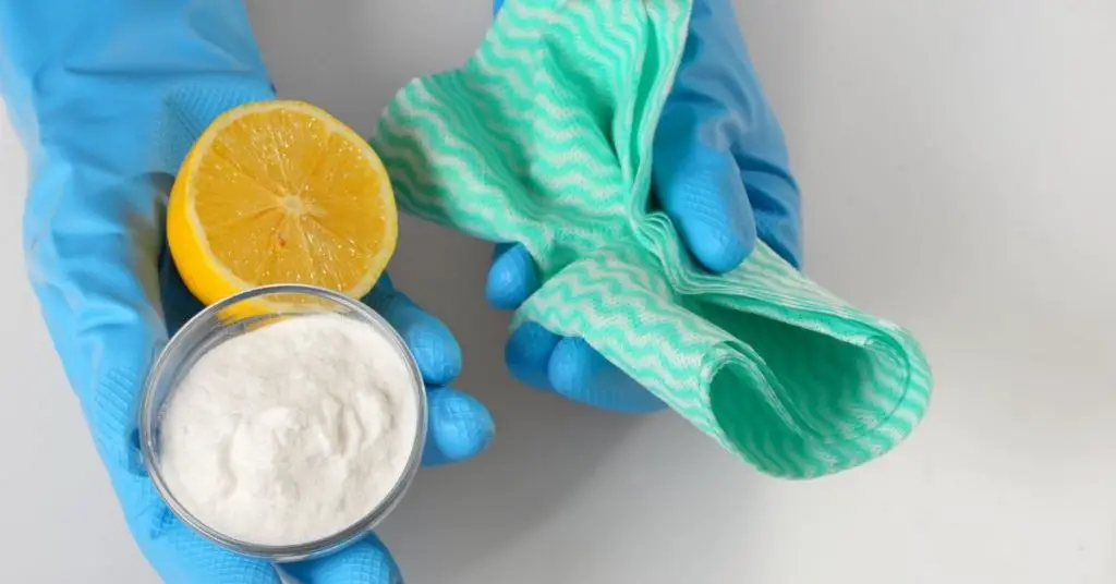 Person wearing gloves holding baking soda, lemon and a cloth to clean with Bicarbonate of soda - Clean and Tidy Living