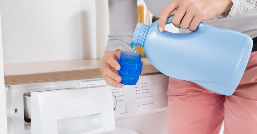 Pouring laundry detergent in a blue cap next to washing machine - difference between bio and non bio