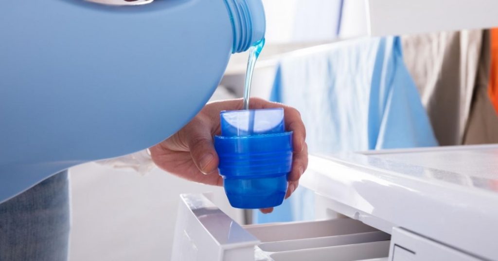 Pouring laundry detergent in a blue cap next to washing machine drawer - difference between bio and non bio