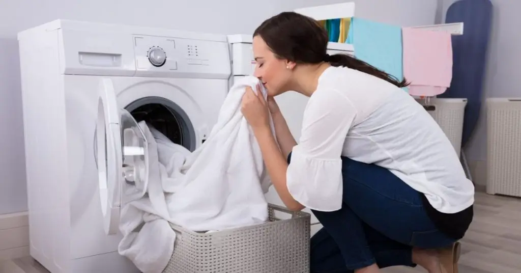 Woman smelling white towels straight out of the washing machine - Clean and Tidy Living